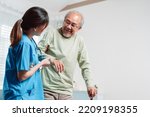 Asian senior elderly man patient doing physical therapy with caregiver. woman nurse helping get up from wheelchair for practice walking with walker at home, practice walk slowly at nursing home care.