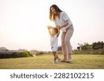 Small photo of Baby taking first steps in park on meadow grass at sunset. Mother supports child to learn walking forward, baby growth and development concept.