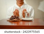 Small photo of Fast breaking meal or iftar dish with muslim man hands praying to Allah. Dates with a glass of mineral water on the table.Traditional Ramadan, fast breaking meal. Ramadan kareem fasting month concept.
