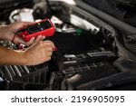 Mechanic doing car inspection, he is testing car battery with tester. Check battery voltage with electric multimeter. Man using multimeter to measure the voltage of the batteries.