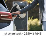 Small photo of The driver of the electric car inserts the electrical connector to charge the batteries. Unrecognizable man attaching power cable to electric car. Electric vehicle Recharging battery charging port.
