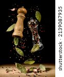 Small photo of Two spice mills with peppercorns and laurel bay leaves on black flying over table. Grinder for spices. Salt and pepper shakers levitation