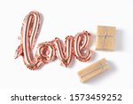 The inscription love in the form of a balloon in pink gold color on a white background. gift boxes of various sizes in craft paper. Flat lay.