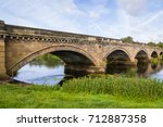 Stone Bridge over The River Trent between Repton and Willington Derbyshire. Showing the river, cloudy sunny blue sky, green folage foreground, reflection of bridge in water.