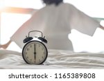 Woman on bed wake up stretching in bedroom with alarm clock at 6.00 a.m. morning. Biological Clock healthcare lifestyle concept