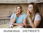 Small photo of Young pretty long-haired girl with pleasure drinks tea and eats pancakes with honey. Fat blonde with undisguised envy looks at what is happening. The concept of a healthy diet, diet, weight loss.