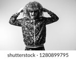 Small photo of Excited cheerful bizarre man posing om white studio background. Stylish funky male with curly hair black and white portrait. Funny guy in tracksuit expressing feelings. Unusual person in sunglasses.