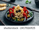 Small photo of Toasts with scrumbled eggs, with two olives portraying eyes, sausages mimic the legs of a spider, and green peas, resembling spider eggs on black plate over galvanized background. Selective focus