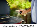 Small photo of Close up on man's hand spraying oil on barbecue gas grill outdoor in the backyard, Preparation for roasting On Grill, summer family picnic, food on the nature.