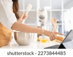 Small photo of Close up of hands with computer in kitchen.Learn cooking online. A young woman is watching cooking tutorial video in the kitchen.Reading recipe while making cookies Following Recipe On Digital Tablet.