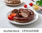 Juicy homemade baked sausage on a plate with mustard and fresh tomatoes.