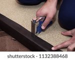 Small photo of Particle board upholstered with brown leather. Repairman using blue stapler and staples to upholster the particleboard, Close up