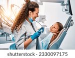 Small photo of A female dentist doctor talks to a small patient, the child shows her teeth and sits in the dental chair.Sunlight.