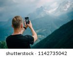 man takes photo of mountain peaks using smartphone