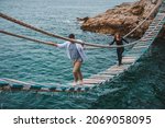 Small photo of couple woman with man walking by shaky suspension bridge crossing sea bay having fun