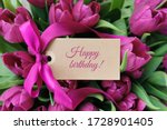 Happy birthday text on label in front of purple flowers - tulips.