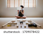 Young asian woman self assembly wooden furniture and read blank white paper to put instruction