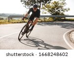 Bearded cyclist in sport clothing, protective helmet and mirrored glasses riding black bike among countryside nature during summer time. Mature man preparing for competitions and races.