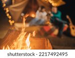 Small photo of Happy couple relaxing in glamping on autumn evening, drinking wine and playing guitar near cozy bonfire. Luxury camping tent for outdoor recreation and recreation. Lifestyle concept