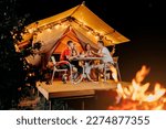 Small photo of Happy group of friends relaxing in glamping and drinking wine on summer evening near cozy bonfire. Luxury camping tent for outdoor recreation and recreation. Lifestyle concept