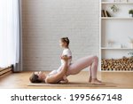 Small photo of Young smiling woman in light pink doing hip workout exercise and Pelvic tilt to pelvic curl pose with litle baby girl sitting on mother's belly as a natural weight to complicate the exercises.