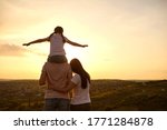 Back view of peaceful family watching sunset at mountains, copy space. Parents with child enjoying evening scenery