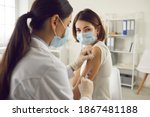 Vaccination, immunization, disease prevention concept. Woman in medical face mask getting Covid-19 or flu vaccine at the hospital. Professional nurse or doctor giving antiviral injection to patient
