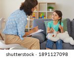 Small photo of Supportive psychologist with clipboard listening to little child during therapy session. Preschool girl feeling at ease in therapist's office sharing her thoughts and concerns