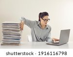 Small photo of Young accountant working on laptop computer sitting at desk with pile of papers. Paperwork vs electronic documents. Storing files in digital database. Having quick convenient access to storage system