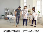 Small photo of Team of doctors of different nationalities in the hospital room helps their patient with a broken ankle, who walks on the cauldrons. Concept of treatment of serious physical injuries.