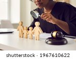 Small photo of Black judge or lawyer looking in magnifying glass at little mom, dad children figures on desk. Family law court case investigation, divorce, joint custody of kid, parental rights deprivation concept