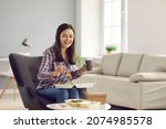 Small photo of Happy woman eating takeout lunch at home. Beautiful young girl sitting in armchair, drinking coffee and enjoying healthy vegetable salad from takeaway food container. Meal delivery service concept