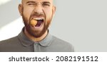 Small photo of Confident, charismatic, handsome man winks his eye and cracks a hard nut. Close up head shot of a young ginger guy demonstrating his healthy teeth and trying to crack a walnut. Dental health concept