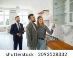 Small photo of Realtor with customers checking apartmnet. Couple examines furniture in kitchen while inspecting house with real estate agent. Friendly male realtor advises young family before buying new home.
