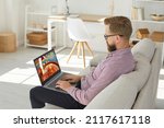 Small photo of Young man sit relax on sofa play casino online on computer. Caucasian male rest at home couch gamble internet on laptop. Entertainment on web. Gambler or gamer Russian roulette.