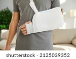 Small photo of Close up of sling on broken arm of man he needs to wear during rehabilitation period. Unknown male patient wearing immobilizer after car accident or after sports injury. Orthopedics concept.