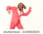 Small photo of Funny man wearing a wacky dinosaur mask having fun at a crazy party. Profile view of a happy young guy in a pink suit and a silly scary ugly masquerade dino mask dancing isolated on a white background
