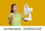 Small photo of Young woman with a fan in her hand is exhausted from the heat, trying to cool off by the fan, oppressive heat, too hot weather and sultriness in summer, flat without air-conditioner concept.
