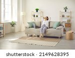 Small photo of Happy lady leaning back on comfy sofa in cozy bright living room in her own apartment. Relaxed woman enjoying free time on quiet weekend or day off and sitting hands behind head on soft couch at home
