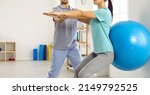 Small photo of Young female patient together with physiotherapist does exercises for back with help of fitball. Cropped image woman perform squats with fitball to get rid of back pain and restore spine health.