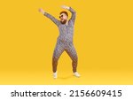 Small photo of Cheerful funny eccentric fat man in good mood is dancing and fooling around on orange background. Overweight bearded man dressed in leopard print jumpsuit is dancing and fooling around. Full length.