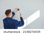 Small photo of Male technician installing surveillance camera on light copy space wall. Back view of repair service worker using screwdriver to fit screws and adjust wall mounted CCTV security dome cam inside house