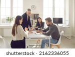 Small photo of Group of positive people dressed in casual clothes discuss plan for cooperation on common project in modern coworking. People write their ideas in notebook sitting at table in bright office.