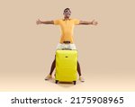 Overjoyed African American man in glasses isolated on brown studio background excited about summer vacation. Smiling biracial guy with suitcase ready for summertime travel or journey.