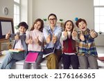 Small photo of Happy teacher with pupils group giving thumbs up. Toothy smiling tutor with elementary or secondary school student looking at camera portrait. Schoolroom interior. Offline education acknowledgment