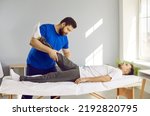 Male physiotherapist work patient after leg trauma help with pain relief and rehabilitation. Therapist or osteopath massage client leg after injury. Recovery and rehab center concept.