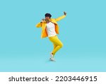 Cheerful funny woman in good mood dancing cheerfully isolated on light blue background. Young stylish African American woman in yellow casual suit, t-shirt, sneakers and sunglasses. Full length.