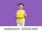Small photo of Positive sympathetic Caucasian school age girl holds dialogue bubble symbolizing communication between children or invitation to chat via Internet standing in purple studio. Networking concept
