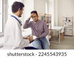 Small photo of Young dark-skinned man complains of dizziness and headache during medical examination. Doctor and patient are sitting on examination couch. Doctor asks man and makes notes on clipboard.