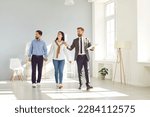 Young couple following a real estate agent who is giving them a tour around a big house, showing all the rooms and telling about all the advantages of living here. Buying house or apartment concept
